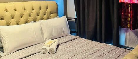 Een net opgemaakt bed met een gestoffeerd hoofdbord, een gewatteerde sprei en opgerolde handdoeken.