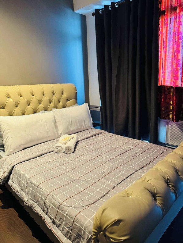 A neatly made bed with a tufted headboard, a quilted bedspread, and rolled towels.