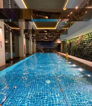 An indoor swimming pool with clear lane markers, surrounded by a modern interior with glass walls and a green wall with plants. - Gramercy Residences Studio Suites  (Makati)