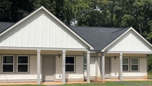 A two-story building with a symmetrical facade, large windows, and a covered porch area. - Luxurious Brand-New 1BR Apartment – Modern and Open floor plan with fire pit! (Jonesboro)