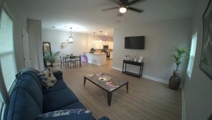 A living room with a sofa, coffee table, and a dining area with chairs. - Luxurious Brand-New 1BR Apartment – Modern and Open floor plan with fire pit! (Jonesboro)