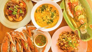 Diversos pratos de frutos do mar, incluindo caranguejo, peixe e uma sopa, servidos sobre uma mesa de madeira.