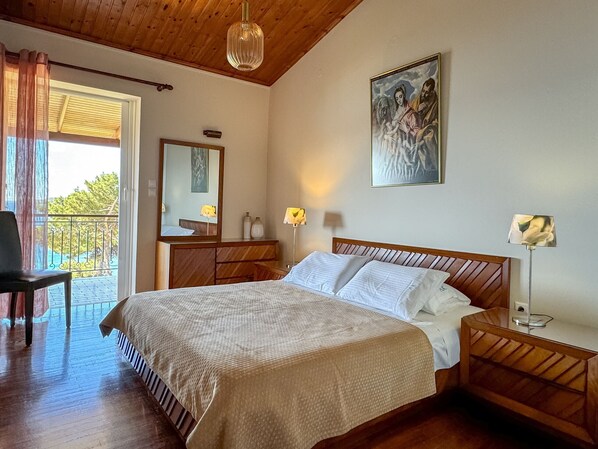 Un dormitorio con una cama de madera, una mesita de noche, un espejo, un cuadro y un balcón con una silla.