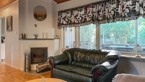 A living room with a leather sofa, a fireplace, and a large window with a view of trees. - Cozy home in Strömsnäsbruk with WiFi (Strömsnäsbruk)