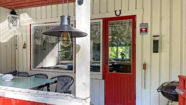 A covered outdoor seating area with a table and chairs, a hanging light fixture, and a red door with a window. - Cozy home in Strömsnäsbruk with WiFi (Strömsnäsbruk)