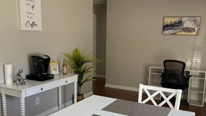 A dining area with a white table and chairs, a ceiling fan, a coffee maker, and a plant. - Cozy & Convenient 2BR Corporate Stay – Ideal for Relocation or Recovery (Jonesboro)