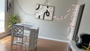 A dining area with a white table and chairs, a painting on the wall, and string lights. - Cozy & Convenient 2BR Corporate Stay – Ideal for Relocation or Recovery (Jonesboro)