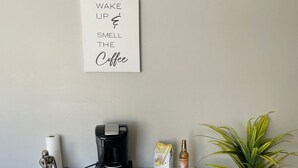 A white desk with a coffee maker, a bag of coffee, a bottle of coffee creamer, and a potted plant. - Cozy & Convenient 2BR Corporate Stay – Ideal for Relocation or Recovery (Jonesboro)