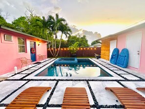 A swimming pool with wooden loungers, a pink building, and a wooden fence. - Salthaus Suite C - Brand NEW Saltwater Pool & Spa, Near Beach, Downtown, Airport (West Palm Beach)