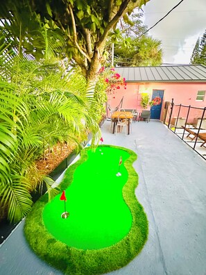 A miniature golf course with a green putting area, a red flag, and a pink building in the background. - Salthaus Suite C - Brand NEW Saltwater Pool & Spa, Near Beach, Downtown, Airport (West Palm Beach)