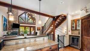 A kitchen with a stone fireplace, wooden counter, and a large window overlooking greenery. - Schweitzer Resort Stay | Deck, Hot Tub & Stunning Views (Sandpoint)