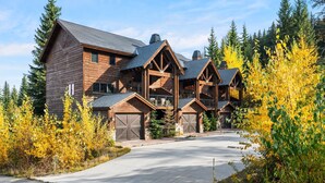 A large log cabin with multiple garage doors, surrounded by trees and a clear sky. - Schweitzer Resort Stay | Deck, Hot Tub & Stunning Views (Sandpoint)