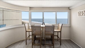 A corner room with a view of the beach, a table with four chairs, and a sign on the window railing. - Gorgeous 3 Bedroom Condo Oceanfront with Pool! (Ocean City)