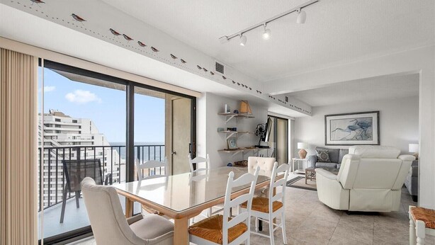 Een moderne woonkamer met een glazen eettafel, witte stoelen, een bank en een balkon met uitzicht op de stad.