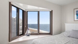 Een slaapkamer met een groot erkerraam met uitzicht op een strand en de oceaan.