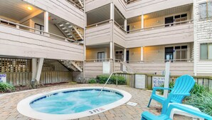 A pool area with a hot tub, lounge chairs, and a staircase leading to upper floors.