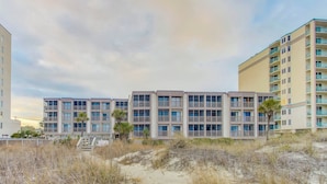 A beachfront hotel with multiple balconies, a sandy beach in front, and a clear sky.