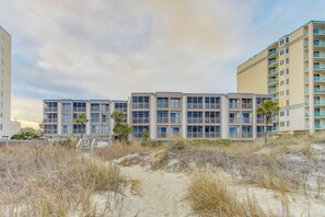 A beachfront hotel with multiple balconies, a sandy beach in front, and a clear sky. - Oceanfront Condo with Screened Oceanfront Balcony + Free Attraction Tickets! (North Myrtle Beach)