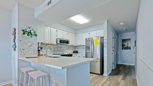 A modern kitchen with white cabinets, a large island with stools, stainless steel appliances, and a marble backsplash.