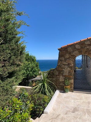 A stone archway leading to a patio with a view of the ocean, surrounded by greenery. - "Les Mimosas", Villa with panoramic sea view and swimming pool (Roquebrune-sur-Argens)