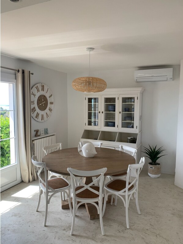 Een eetgedeelte met een ronde houten tafel, witte stoelen, een grote wandklok en een kast met glazen deuren.