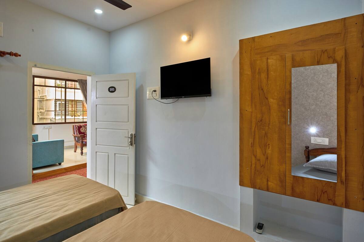 A bedroom with a bed, a TV mounted on the wall, a wooden wardrobe, and a door leading to a balcony.
