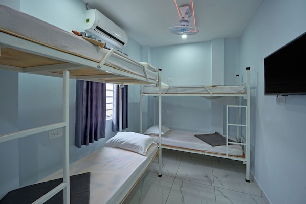 A dormitory room with bunk beds, an air conditioning unit, a ceiling fan, and a television on the wall. - Panakal Residency (Kochi)