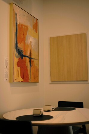 Un salón de conferencias con una mesa redonda, dos sillas, una taza de café y dos cuadros en la pared.