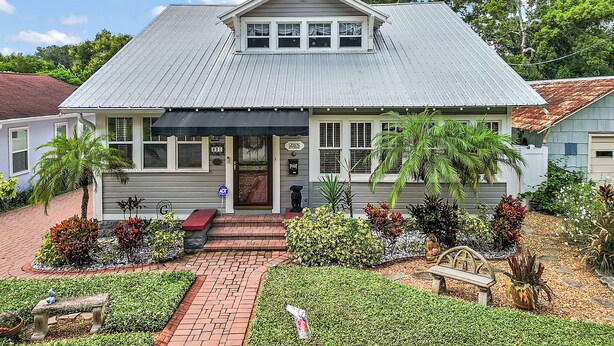 A two-story building with a gabled roof, a front porch, and a small garden with a bench and various plants. - "The Hanscom House" 8 MIN walk to DT! (Mount Dora)