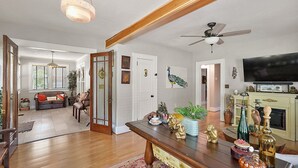 A spacious living room with a wooden floor, a dining table with decorative items, a television, and a fireplace. - "The Hanscom House" 8 MIN walk to DT! (Mount Dora)