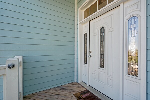 A corner of a house with light blue siding, a white door with glass panels, and a wooden deck.