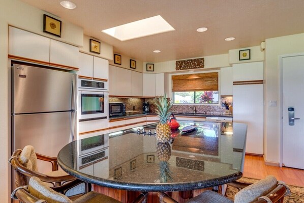 A modern kitchen with a central glass-top island, stainless steel appliances, and a decorative pineapple centerpiece.