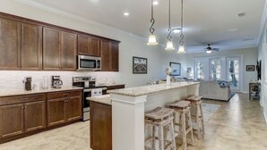 Una cocina amplia con armarios de madera, una isla central con taburetes y un gran ventanal que proporciona luz natural.