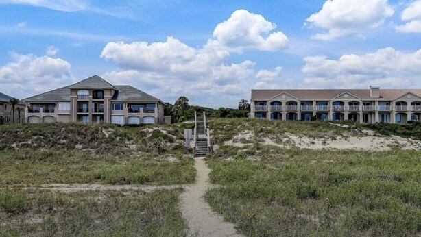 Un sendero que lleva a un edificio con varios balcones y una playa arenosa al fondo.