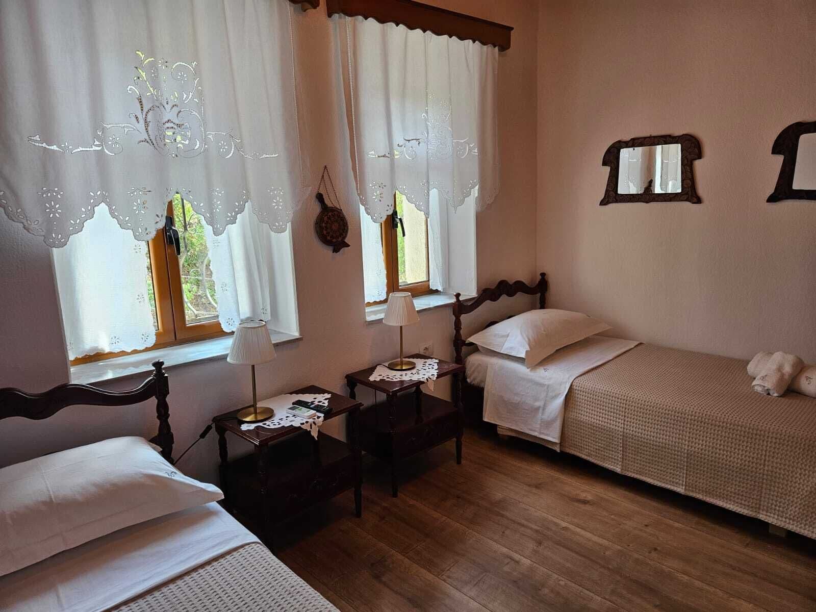 A room with two single beds, a wooden floor, and a window with lace curtains.