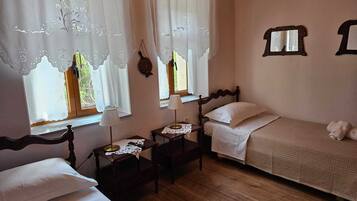 A room with two single beds, a wooden floor, and a window with lace curtains.
