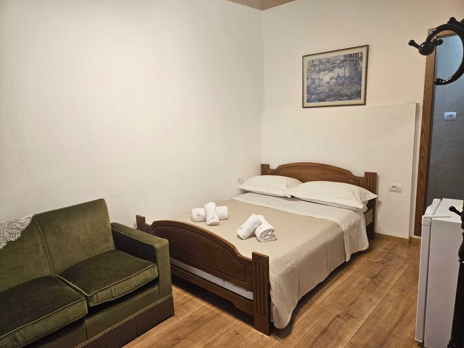 Une petite pièce bien rangée, avec un lit simple, un canapé vert, un plancher en bois et un tableau accroché au mur.