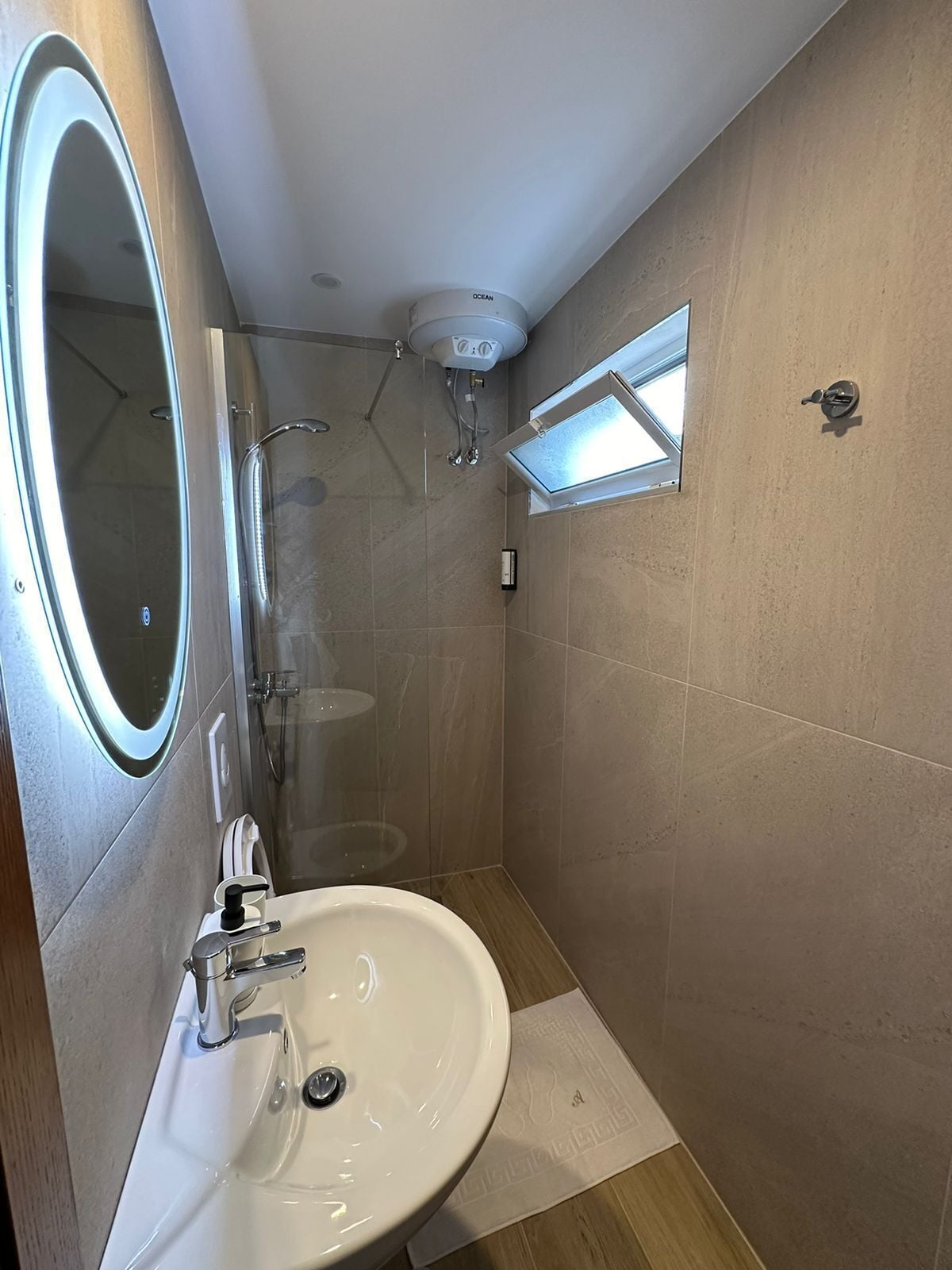 A modern bathroom with a glass-enclosed shower, a white sink, and a mirror with a light.