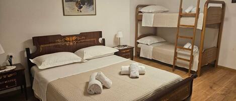 A bedroom with a large bed, a smaller bunk bed, a nightstand, a bedside table, and a wall-mounted painting.