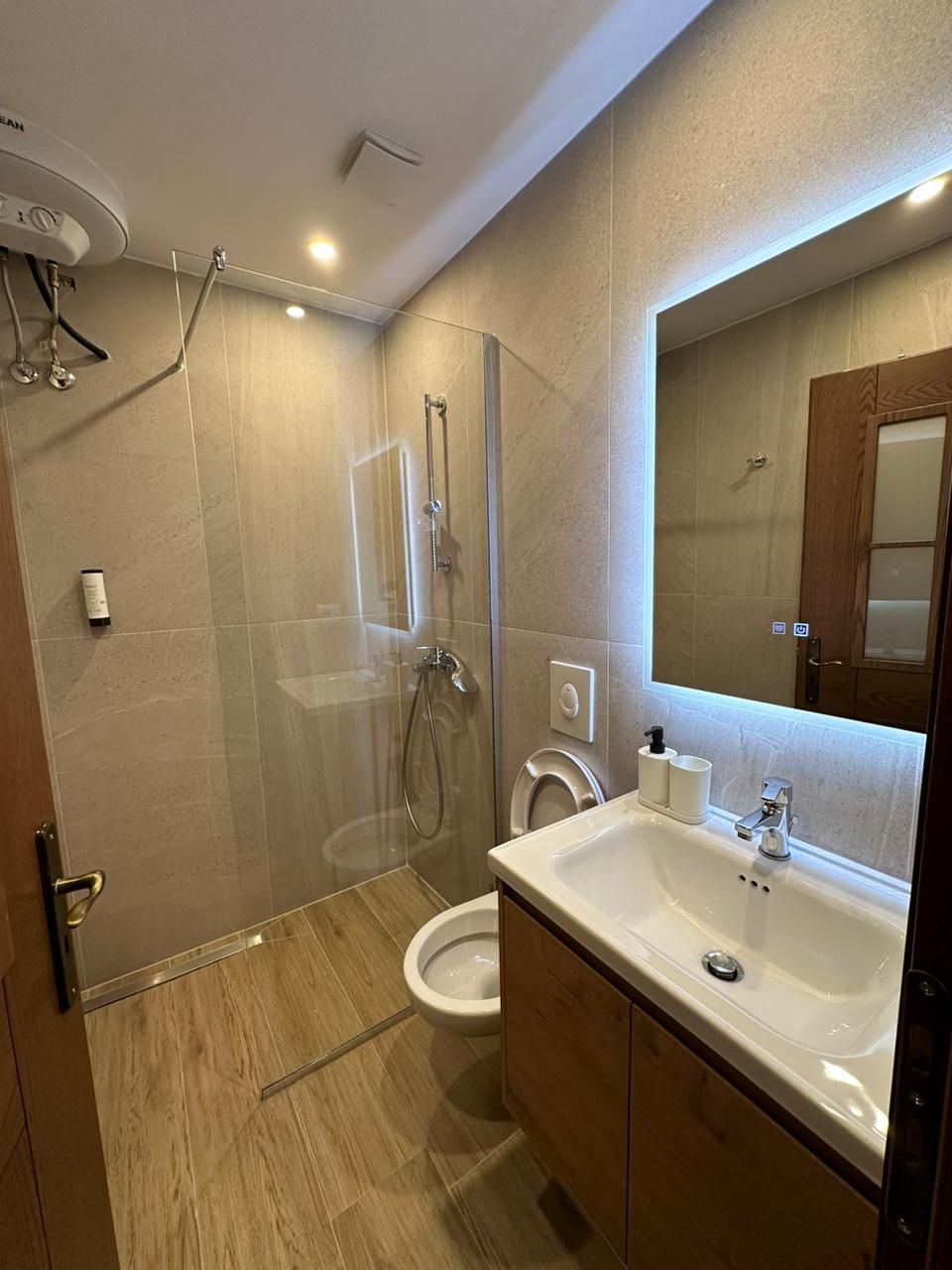 A modern bathroom with a glass-enclosed shower, a white sink, and a large mirror.