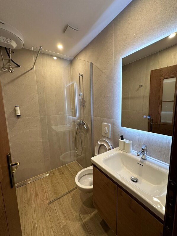 A modern bathroom with a glass-enclosed shower, a white sink, and a large mirror.