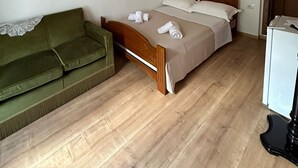 Une pièce avec un plafond en bois, un lit doté d’une tête de lit en bois, un canapé vert et un réfrigérateur blanc.