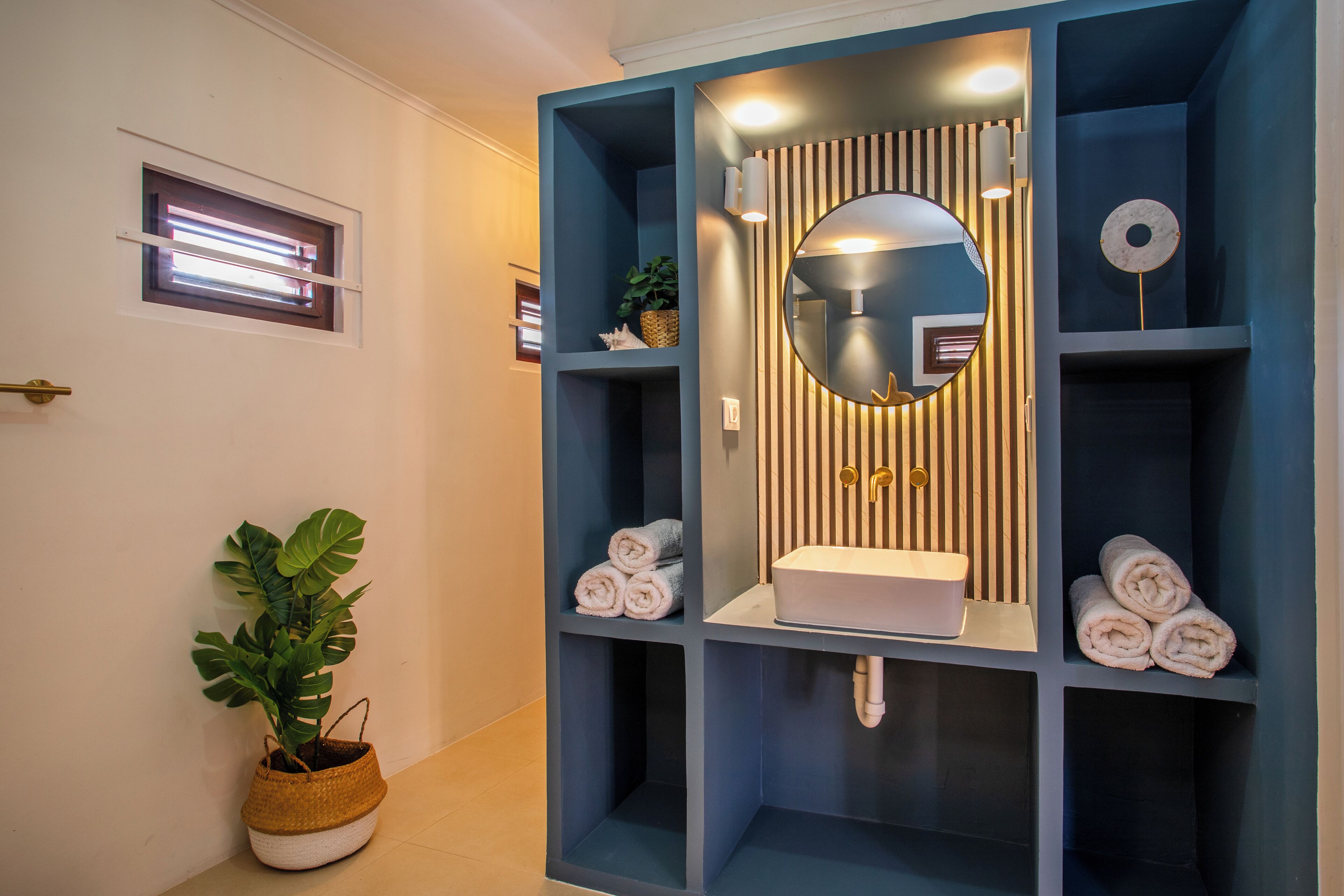 A modern bathroom with a built-in sink, a large mirror, and shelves with towels.
