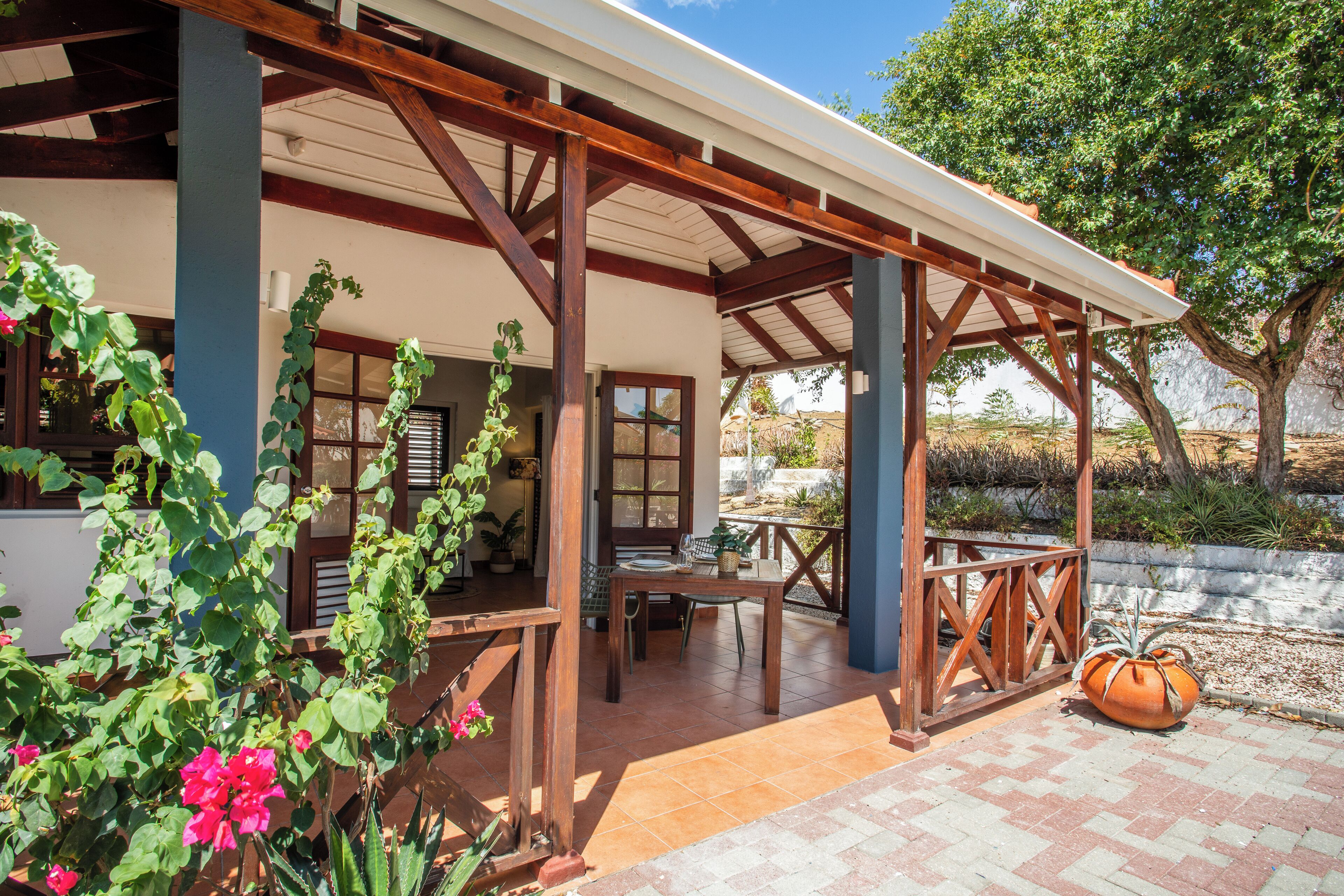 A covered patio area with a wooden pergola, a table, and chairs.