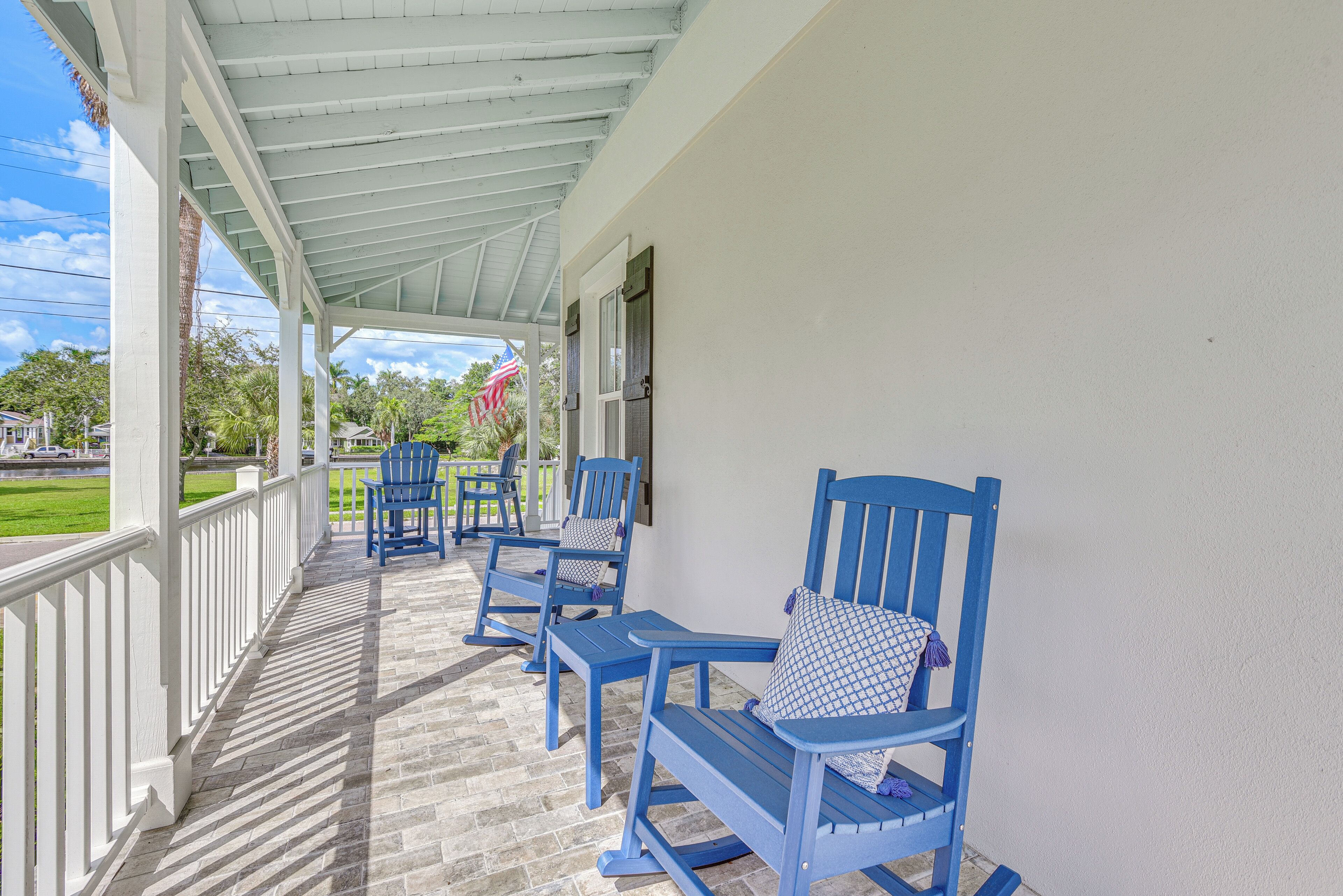 A covered porch with blue Adirondack chairs and a white railing.