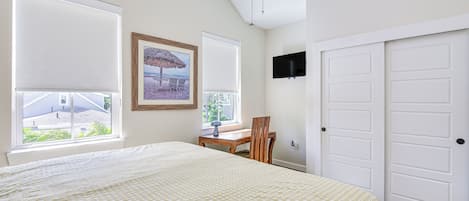 A bedroom with a large bed, a desk, a chair, a TV, and a window with a view of a building.