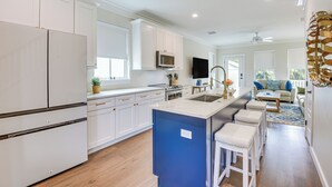 A modern kitchen with white cabinets, a blue island, and a dining area with a sofa and coffee table. - 1 Mi to Riverwalk: Brand New Bradenton Home (Bradenton)