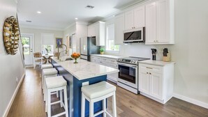A modern kitchen with white cabinets, a central island with bar stools, a built-in oven, and a microwave. - 1 Mi to Riverwalk: Brand New Bradenton Home (Bradenton)
