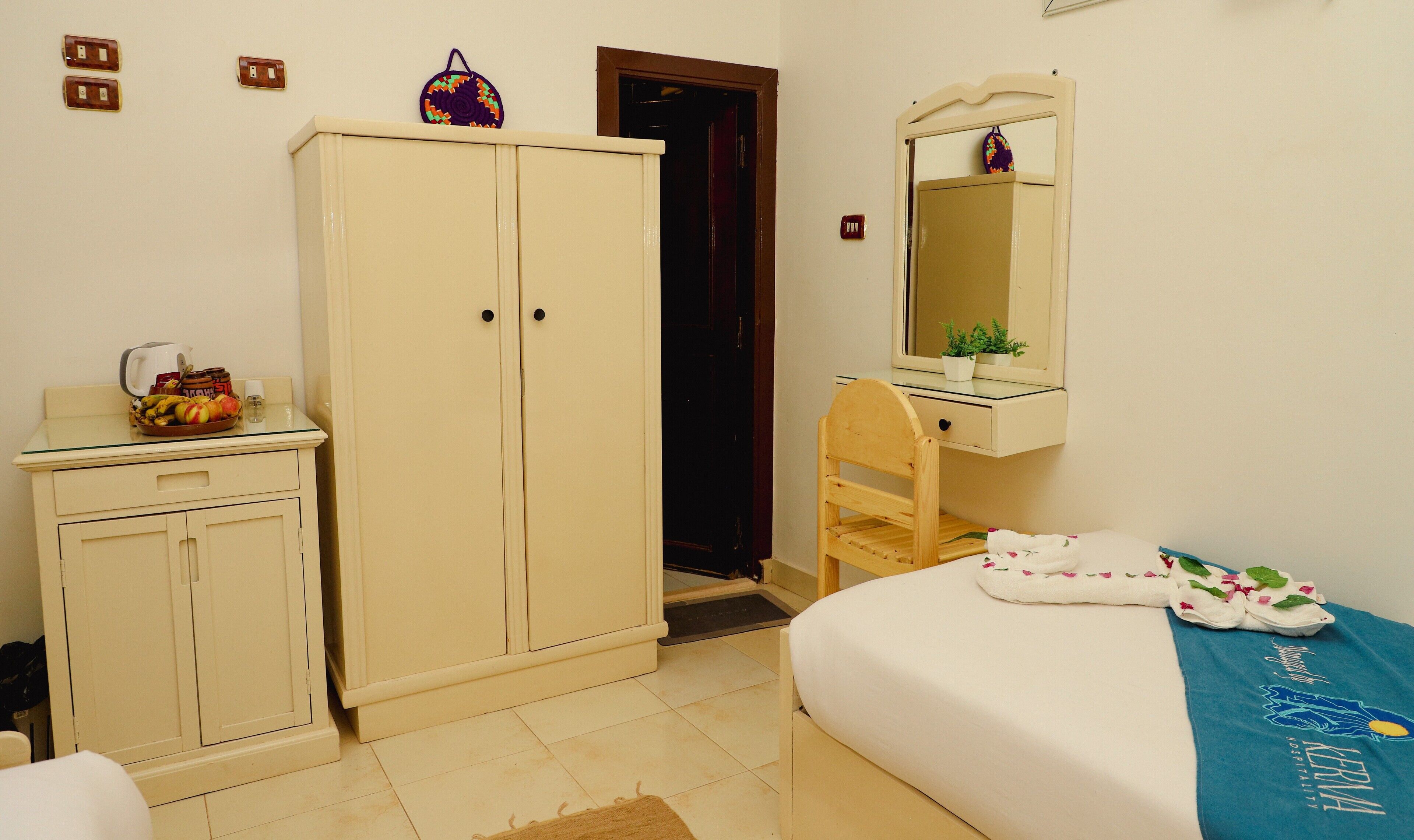 A bedroom with a bed, a wooden chair, a wardrobe, a mirror, and a small table with a bowl of fruit.