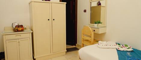 A bedroom with a bed, a wooden chair, a wardrobe, a mirror, and a small table with a bowl of fruit.